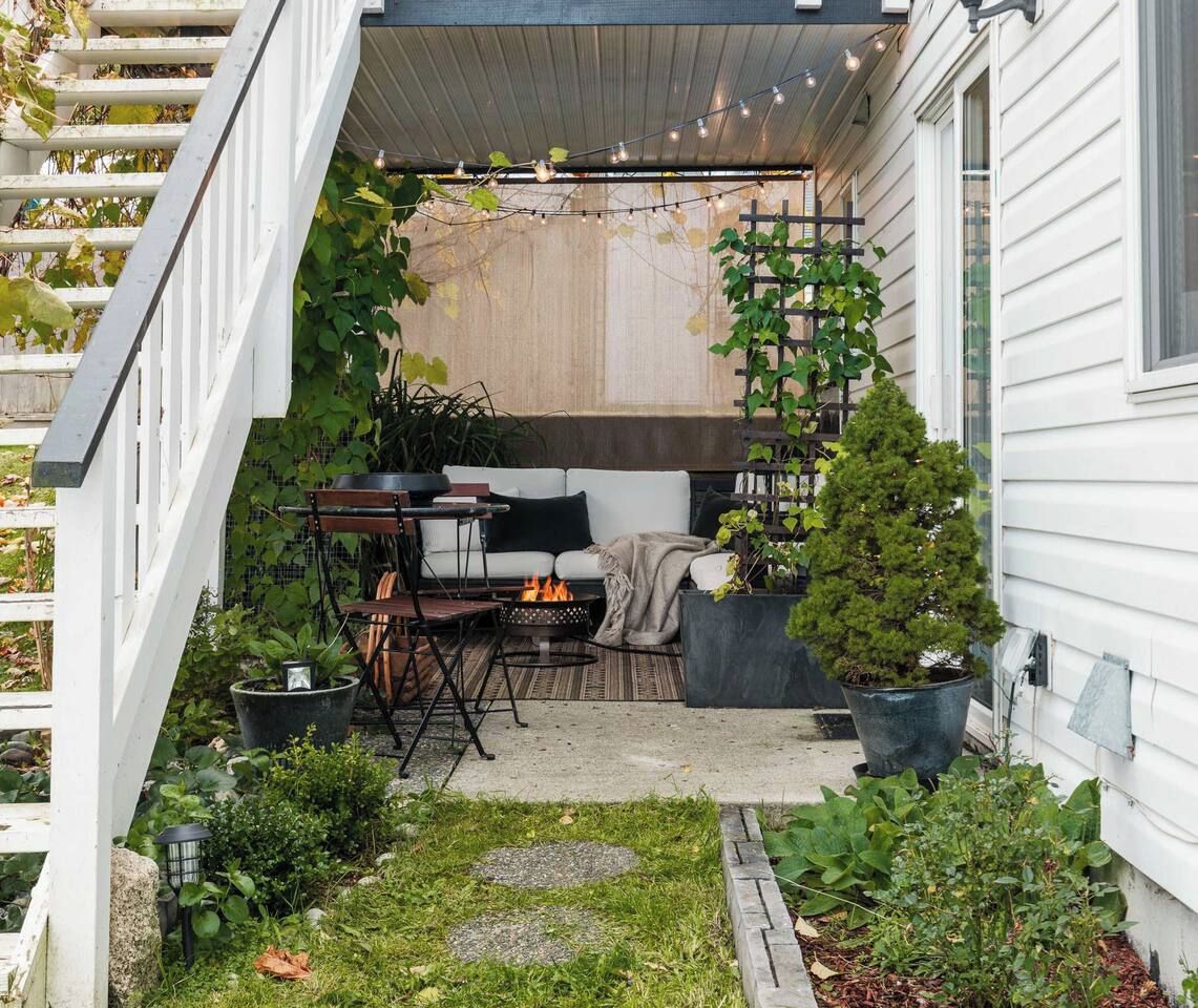 Un espace extérieur aménagé, abrité et doté d’un canapé, de chaises, d’un petit foyer et de plantes en pot.