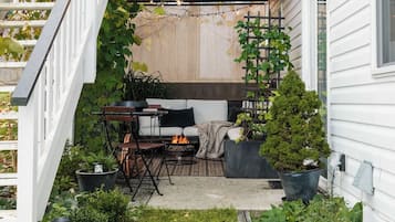 Un espace extérieur aménagé, abrité et doté d’un canapé, de chaises, d’un petit foyer et de plantes en pot.