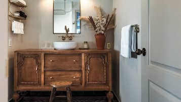 Une salle de bain avec un meuble-lavabo en bois, un grand miroir, deux appliques murales, un porte-serviettes et un tapis à motifs.