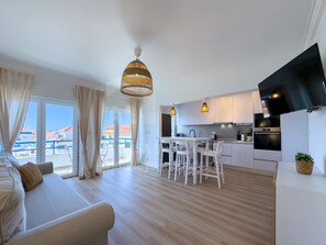 A modern kitchen with white cabinets, a dining area with a white table and chairs, and a large window with curtains. - Barbosa s House by Acasadascasas (Mafra)