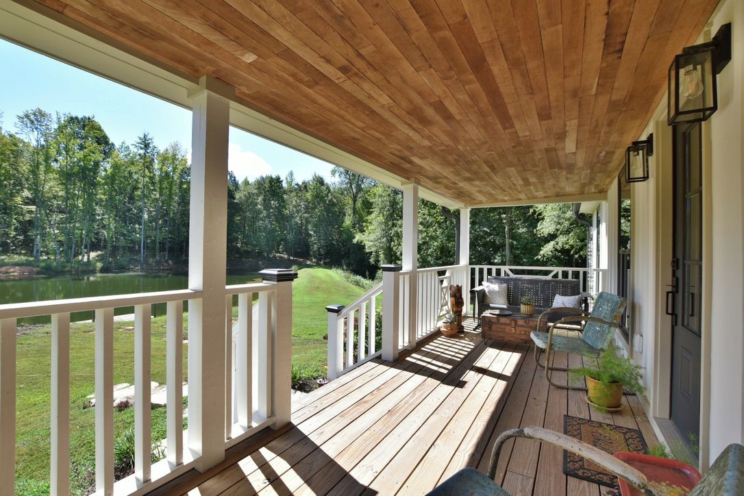 A wooden deck with white railings, outdoor furniture, and a view of a lake surrounded by trees.