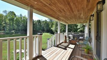 A wooden deck with white railings, outdoor furniture, and a view of a lake surrounded by trees.
