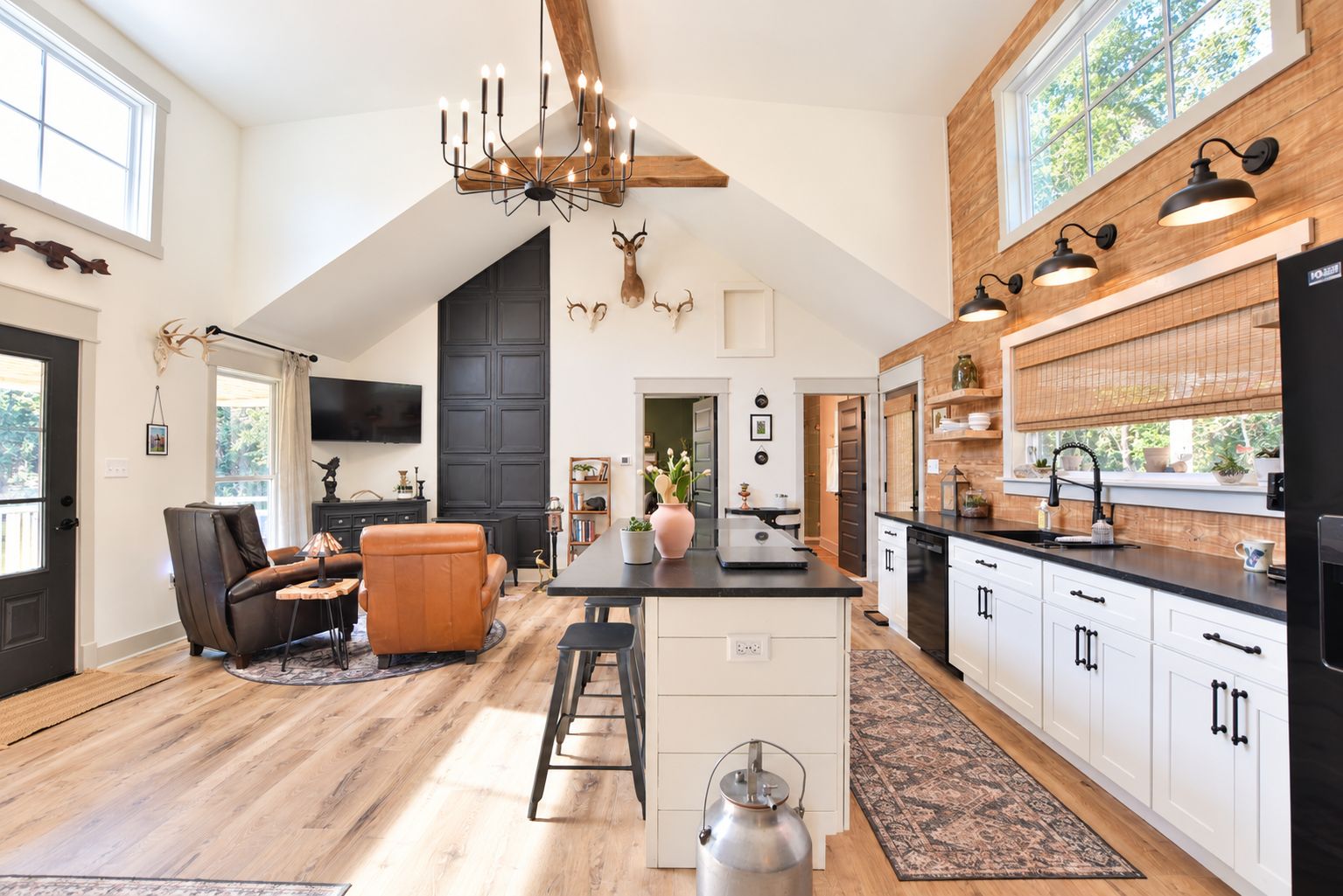 A spacious kitchen with a central island, wooden flooring, and a large chandelier.