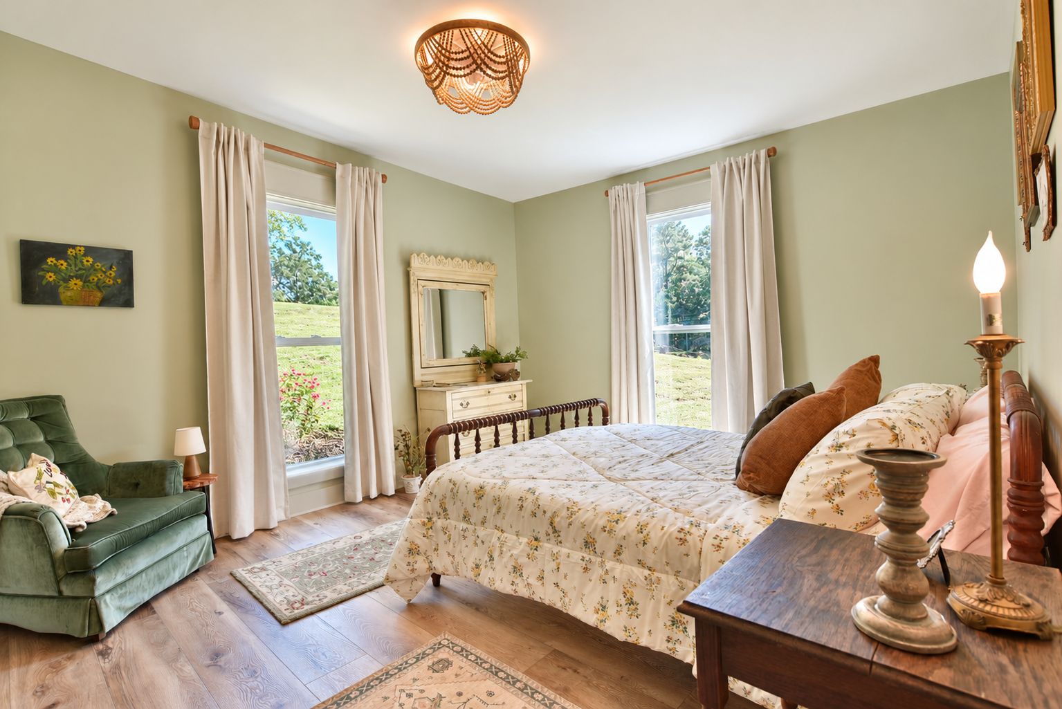 A bedroom with a bed, a dresser, a mirror, a green armchair, and a window with curtains.