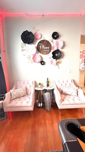 Habitació amb un sofà rosa, una taula rodona petita amb una ampolla i vasos, i una decoració mural amb el text 'The Phan Family'.
