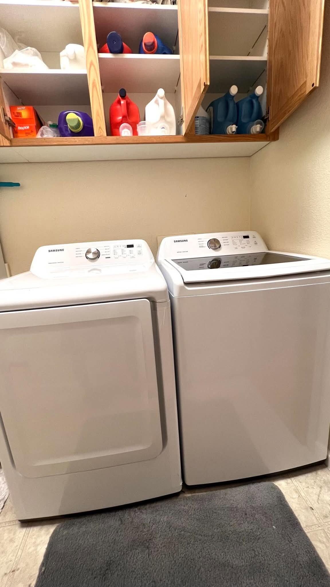 A laundry area with two front-loading washing machines and a shelf above containing various items.
