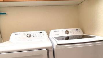 A laundry area with two front-loading washing machines and a shelf above containing various items.