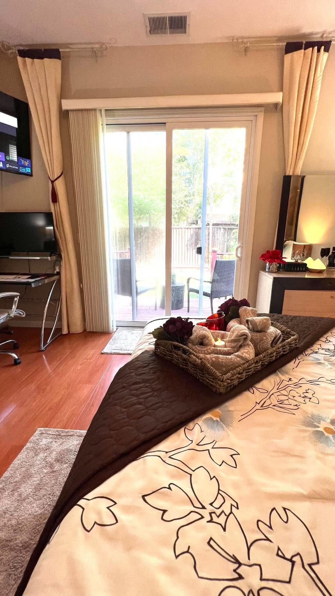 Una habitación de hotel con una cama, un escritorio, un televisor y un ventanal corredera al exterior.