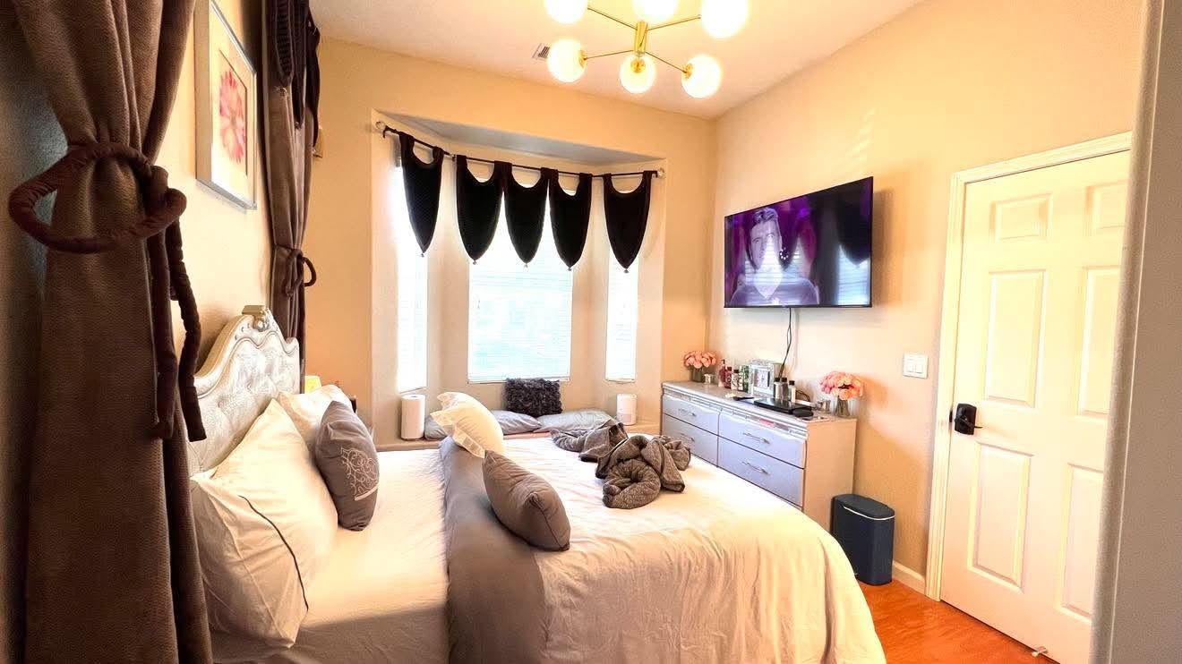 A bedroom with a bed, a dresser, a television, and a window with curtains.