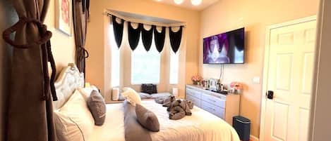 A bedroom with a bed, a dresser, a television, and a window with curtains.