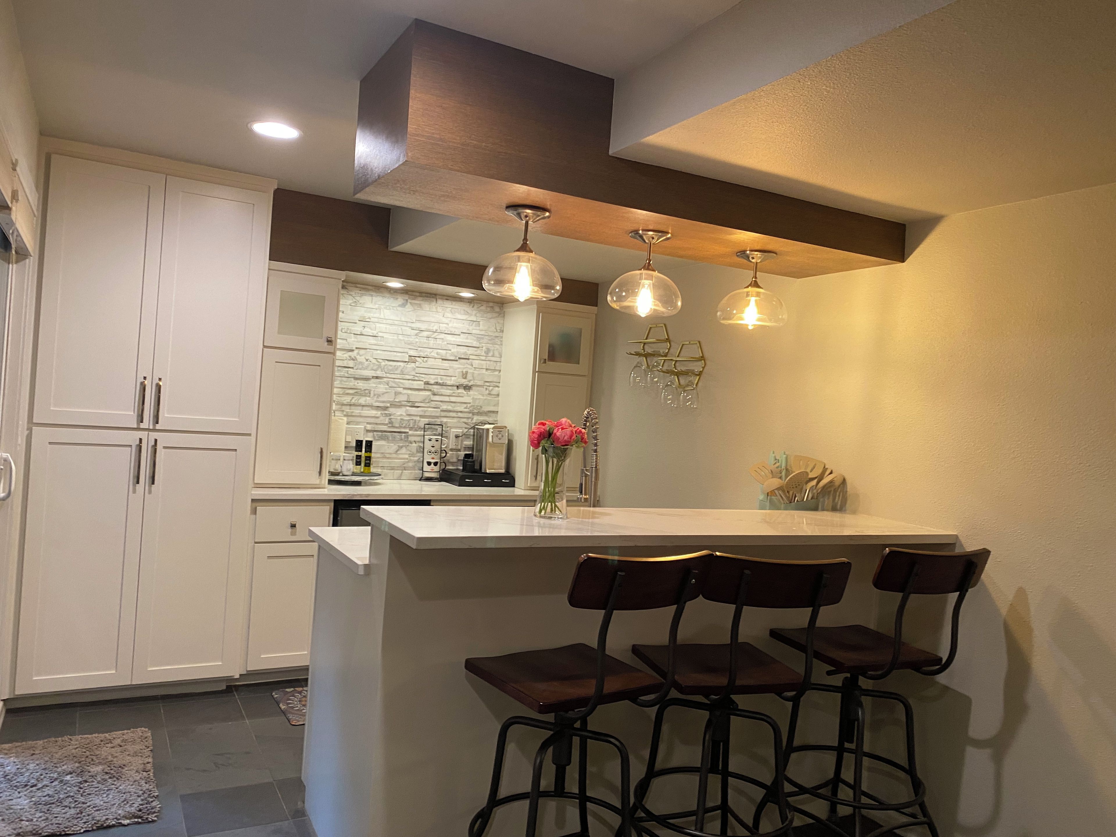 A kitchen with white cabinets, a marble backsplash, and a bar area with stools.