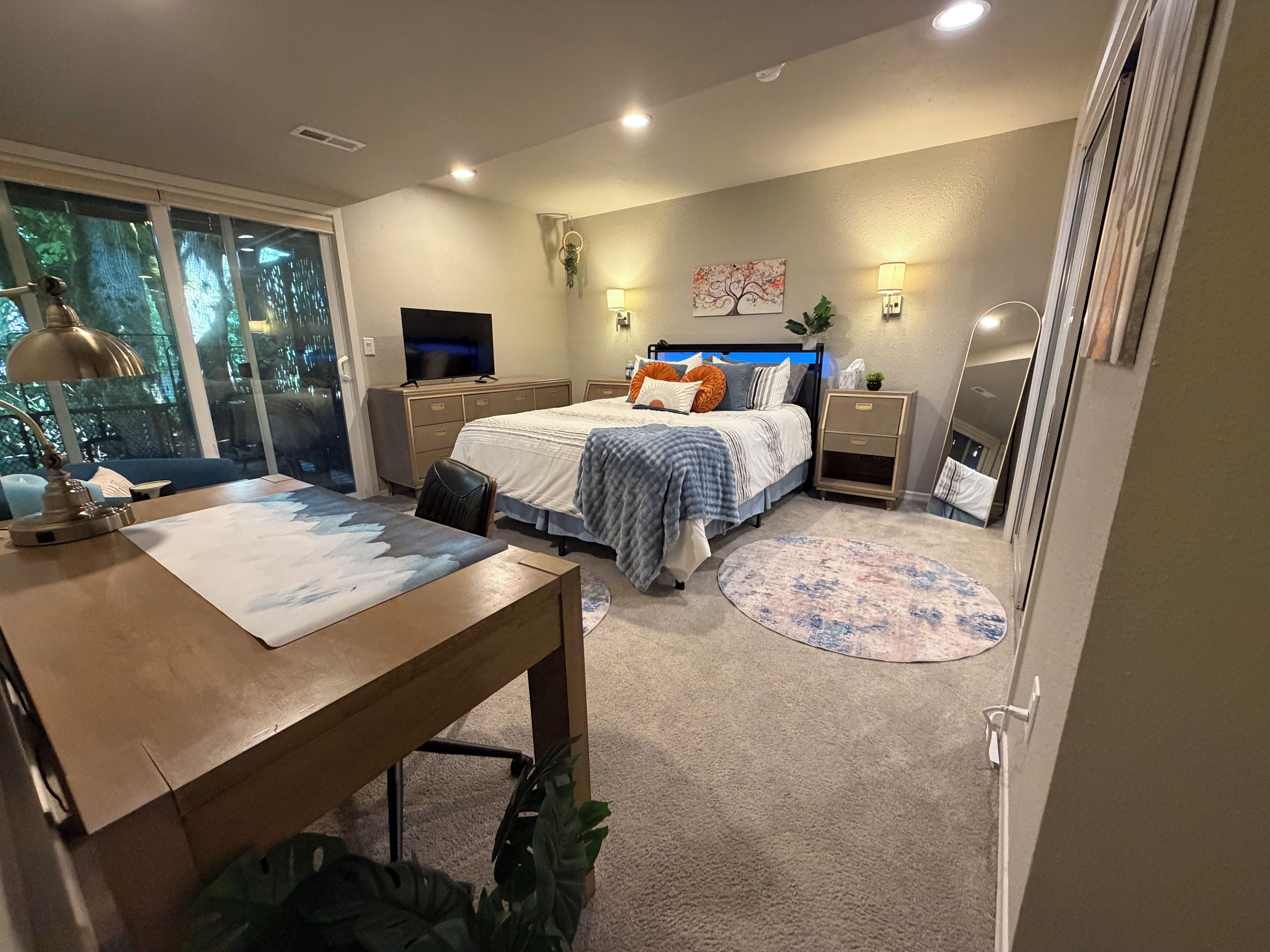 A bedroom with a bed, bedside tables, a desk, a chair, a television, and a window with a view of trees.