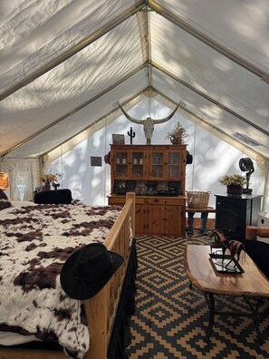 A tent interior with a bed, wooden cabinet, and a table with a decorative item.