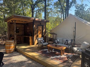 A rustic cabin with a wooden exterior, a small porch, and a tented area with seating. - Cowboy-Themed Tent Getaway (Honey Grove)