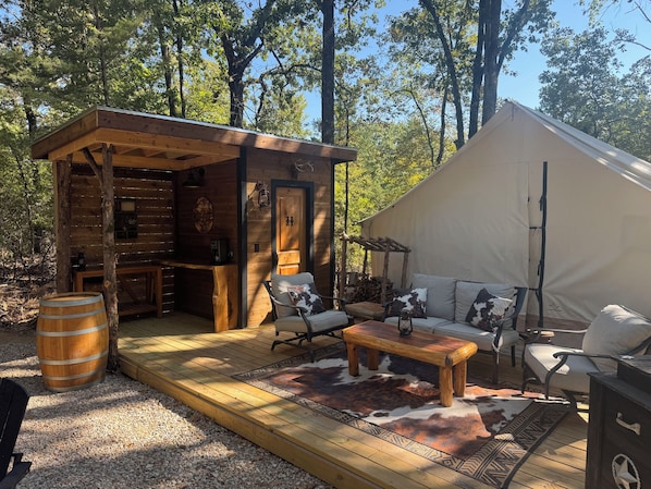 A rustic cabin with a wooden exterior, a small porch, and a tented area with seating.