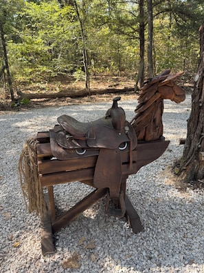 A rustic wooden horse sculpture with a saddle and bridle, set on a gravel path in a wooded area. - Cowboy-Themed Tent Getaway (Honey Grove)
