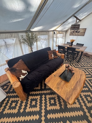 A tented room with a sofa, wooden coffee table, and a dining table with chairs. - Cowboy-Themed Tent Getaway (Honey Grove)