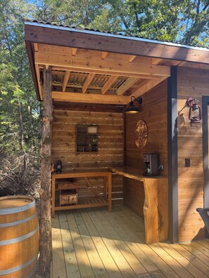 A wooden cabin with a wooden deck, a small window, a wall-mounted lantern, and a rustic bar area.