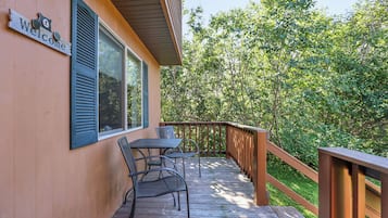 Une terrasse en bois avec une table et des chaises, une pancarte « Bienvenue » et une vue sur une zone boisée.