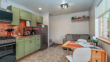 Une cuisine compacte avec des meubles de couleur verte, un réfrigérateur, une cuisinière et un coin repas comprenant une table et des chaises.