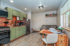 A compact kitchen with green cabinets, a refrigerator, a stove, and a dining area with a table and chairs.
