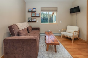A living room with a brown sofa, a wooden coffee table, a white armchair, and a TV mounted on the wall. - Take a load off and instantly improve your mood (Seward)