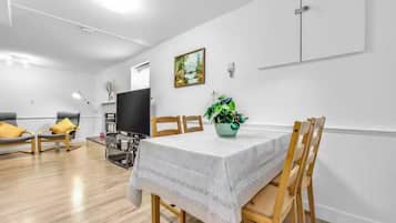 Comedor con una mesa preparada para cuatro personas, sillas de madera, televisor y una planta en maceta.