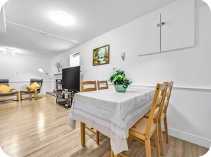 Een eethoek met een tafel voor vier personen, omringd door houten stoelen, een televisie en een potplant.