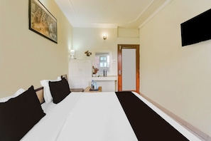 Quarto de hotel com uma cama grande, mesa de cabeceira com abajur, pequena mesa com um vaso e porta para um banheiro.