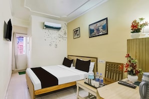 Quarto de hotel com uma cama, uma mesa com chaleira, xícaras e controle remoto.