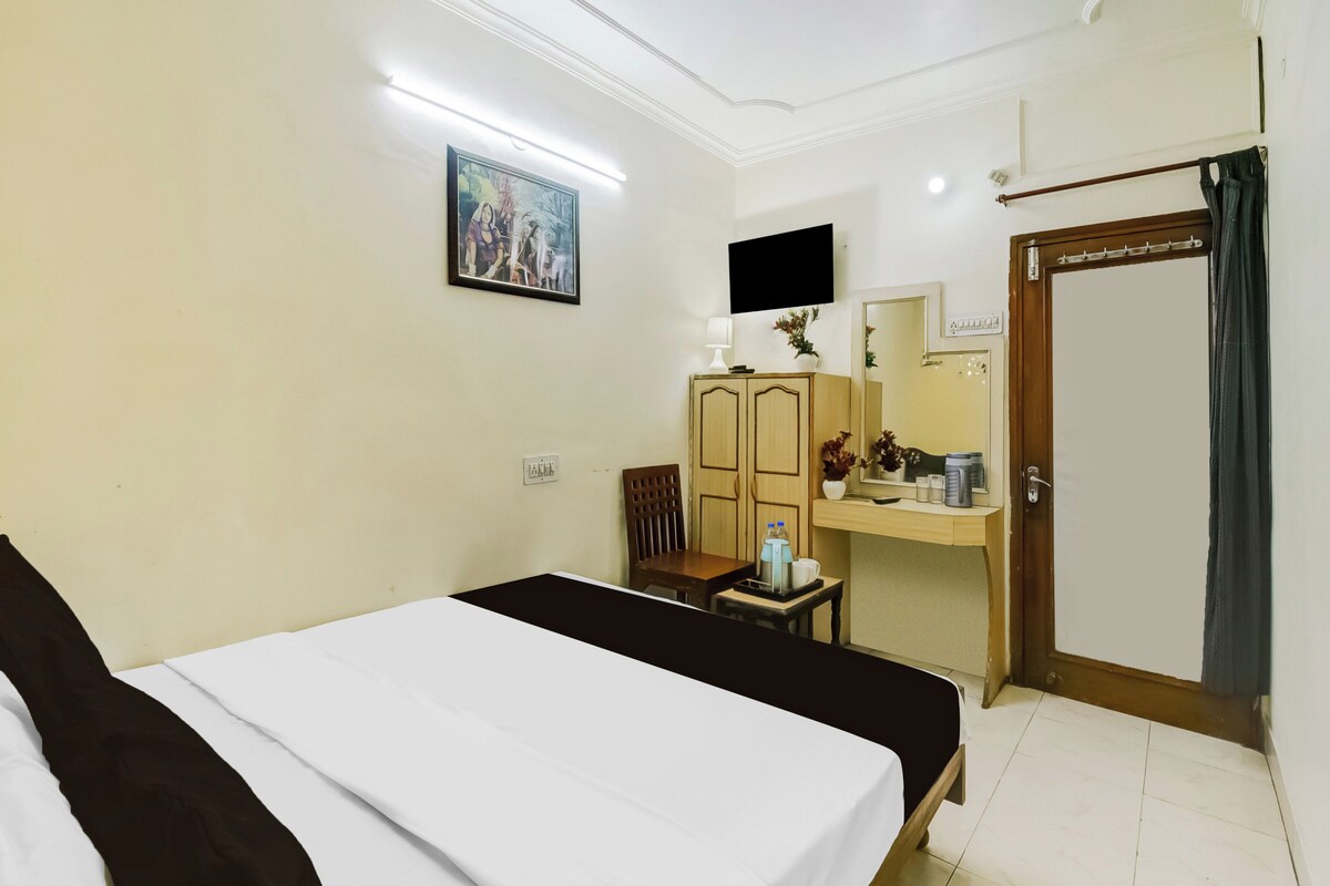 Habitación de hotel con cama, escritorio con silla, armario, televisor montado en la pared y puerta con cortina.