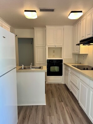 A kitchen with white cabinets, a built-in oven, a refrigerator, and a countertop with a sink. - Perfect Transition Home (Plano)