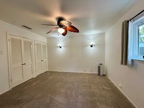 Une pièce dotée d’un ventilateur de plafond, de deux lampes fixées au mur, d’une fenêtre avec des rideaux et d’un plancher recouvert de moquette.