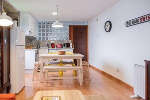 Una cocina con mesa de madera, armarios blancos y una ventana con vidrio emplomado.