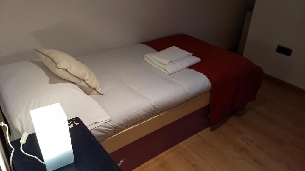 Un lit simple avec une couverture rouge, un oreiller blanc et une couverture blanche pliée au pied du lit.