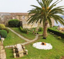 Un edificio de piedra con un sendero empedrado que lleva a una palmera y un jardín circular.