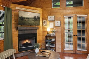 Ein gemütliches Zimmer mit Kamin, Holzwänden, einer Bank, einem Tisch mit Büchern und einer Tür mit Jalousien.