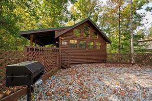 Ein rustikales Blockhaus mit überdachter Veranda, Grill und einem Schotterweg.