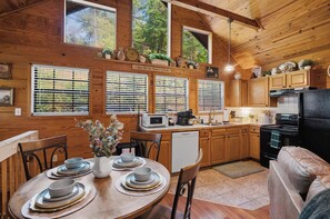 A cozy kitchen with wooden cabinets, a dining table set with plates and bowls, and a sign above the windows that reads 'I Kiss Better Than I Cook'. - Hot Tub-Fireplace-Private-Honeymoon-Hiking-Relax (Sevierville)
