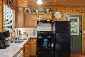 A kitchen with wooden cabinets, a black refrigerator, a stove, and a clock on the wall. - Hot Tub-Fireplace-Private-Honeymoon-Hiking-Relax (Sevierville)
