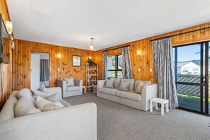 Ein gemütliches Wohnzimmer mit Holzwänden, einer Sofagarnitur, einem Couchtisch und einem Bücherregal.