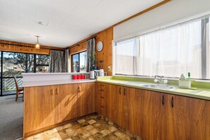 Eine Küche mit Holzschränken, einem großen Fenster mit Vorhängen, einer Spüle und einer Arbeitsplatte mit diversen Gegenständen.