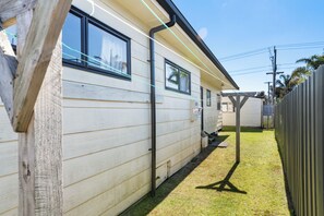 A single-story mobile home with a front porch, a small attached garage, and a fenced backyard. - Kiwi Comfort - Whangamata Holiday Home (Whangamata)