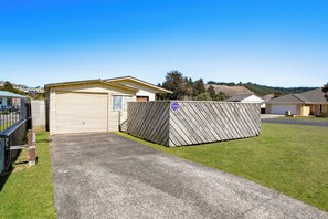 A single-story building with a garage door, a fenced area, and a clear sky. - Kiwi Comfort - Whangamata Holiday Home (Whangamata)