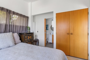 Une chambre à coucher avec un lit, une armoire en bois, une commode et une salle de bain visible à travers une porte ouverte.