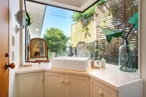 Une salle de bain avec un grand miroir, un lavabo et une fenêtre donnant sur un paysage verdoyant.