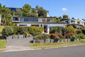 A modern two-story house with a balcony, surrounded by a well-maintained garden and a driveway. - Harbour House - Whangamata Holiday Home (Whangamata)