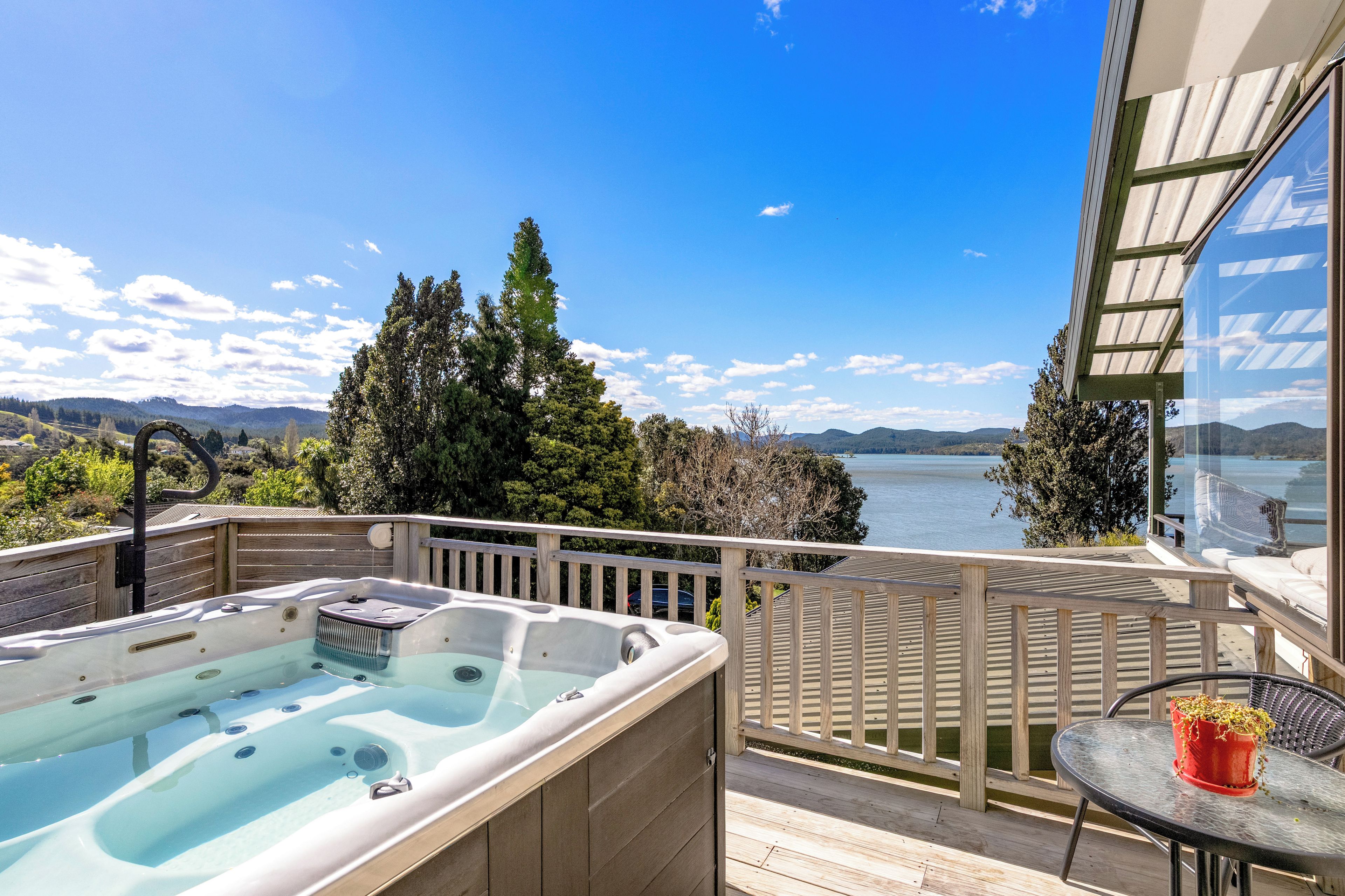 A hot tub on a wooden deck with a view of a lake and mountains.
