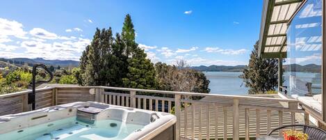 A hot tub on a wooden deck with a view of a lake and mountains.