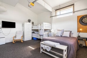 A compact room with a bunk bed, a desk with a lamp, a television, and a dartboard. - Harbour House - Whangamata Holiday Home (Whangamata)